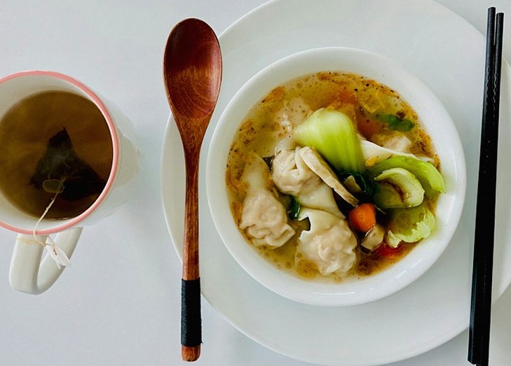 青菜と餃子の入ったスープ、お茶の湯のみ、箸とスプーン